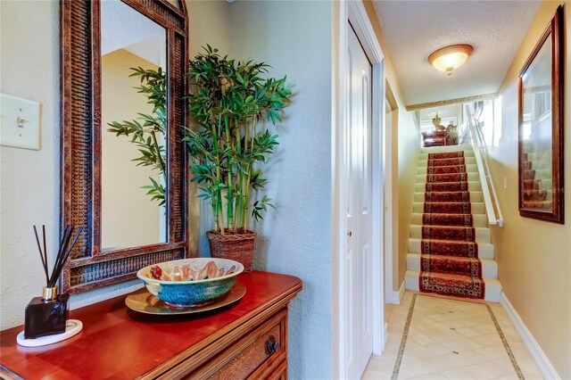 corridor featuring stairs, a textured ceiling, and baseboards