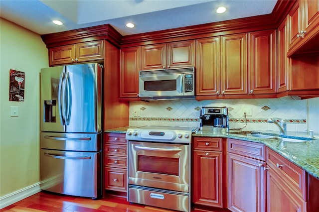 kitchen with light stone counters, stainless steel appliances, backsplash, a sink, and baseboards