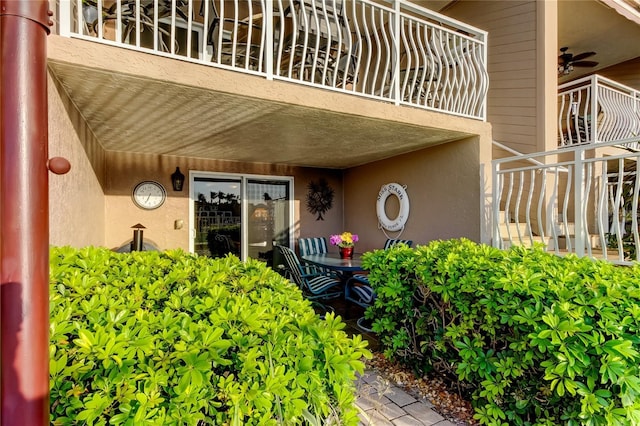 entrance to property featuring a balcony, a ceiling fan, and stucco siding