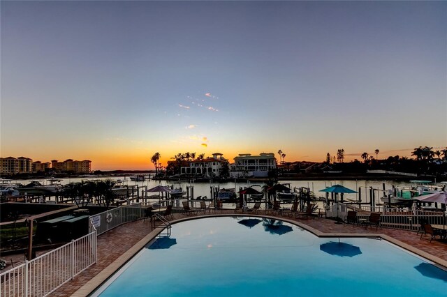 pool at dusk with a water view, fence, and a community pool