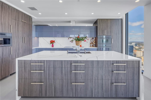 kitchen with light stone counters, visible vents, a large island with sink, and modern cabinets