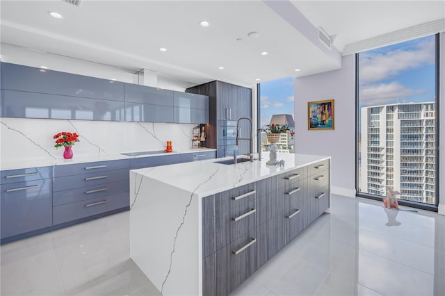 kitchen featuring decorative backsplash, modern cabinets, a large island with sink, floor to ceiling windows, and a sink