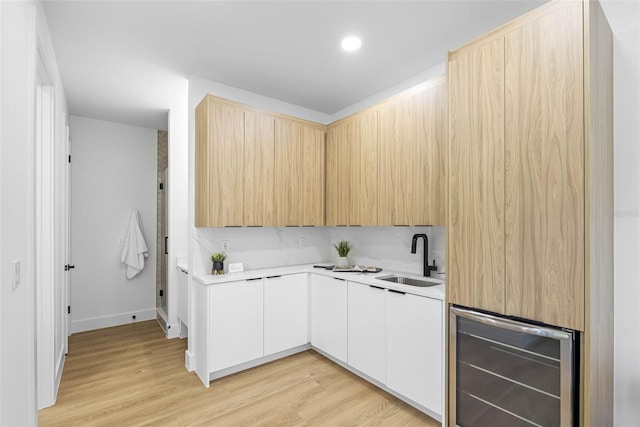 kitchen featuring wine cooler, light countertops, white cabinetry, a sink, and modern cabinets