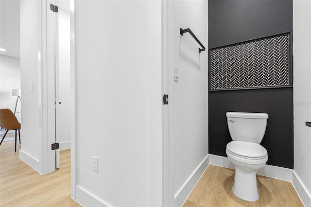 bathroom featuring an accent wall, baseboards, toilet, and wood finished floors