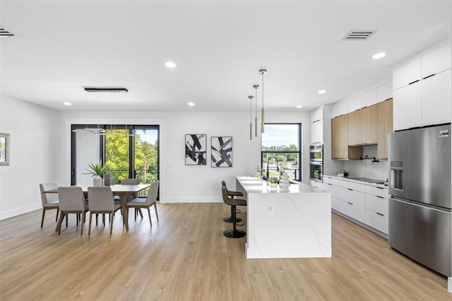 kitchen featuring white cabinets, an island with sink, modern cabinets, stainless steel appliances, and pendant lighting