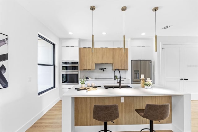 kitchen featuring appliances with stainless steel finishes, light countertops, white cabinets, and an island with sink