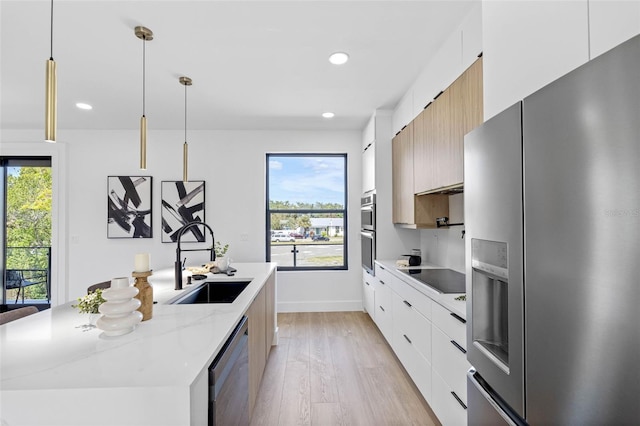 kitchen with white cabinetry, stainless steel appliances, a sink, and decorative light fixtures