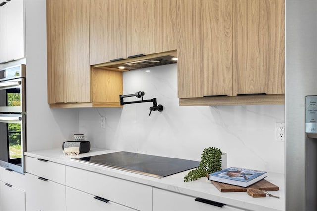 kitchen featuring double oven, black electric stovetop, light brown cabinets, white cabinets, and decorative backsplash