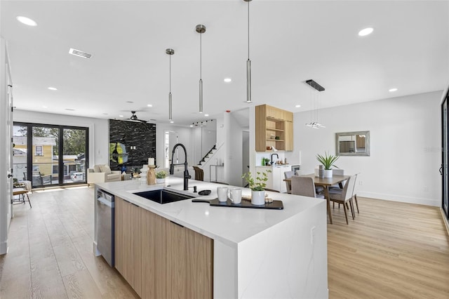 kitchen with pendant lighting, light wood finished floors, open floor plan, a kitchen island with sink, and a sink