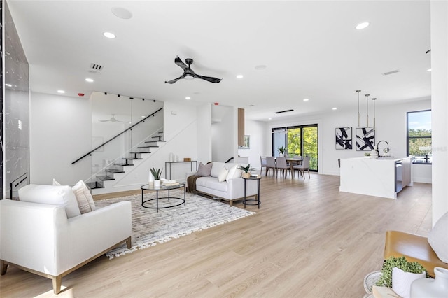 living room with light wood-style flooring, stairs, visible vents, and a wealth of natural light