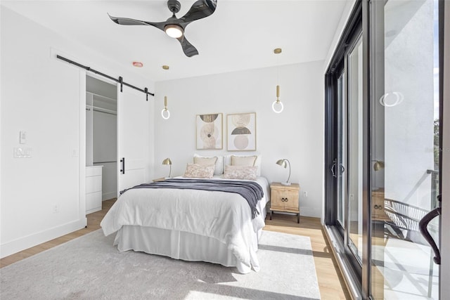 bedroom featuring ceiling fan, a barn door, light wood-style flooring, and baseboards