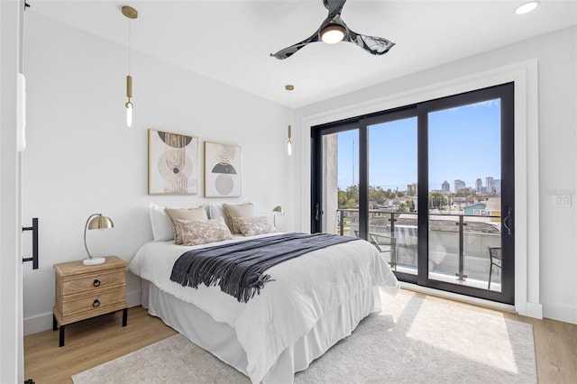 bedroom with light wood finished floors, baseboards, a ceiling fan, access to outside, and a city view