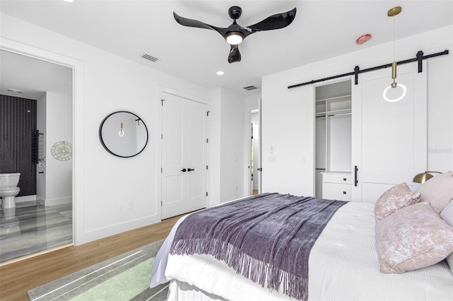 bedroom featuring two closets, visible vents, a barn door, wood finished floors, and baseboards