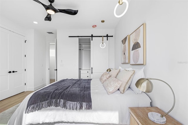 bedroom featuring a barn door, visible vents, a ceiling fan, light wood-style flooring, and a closet