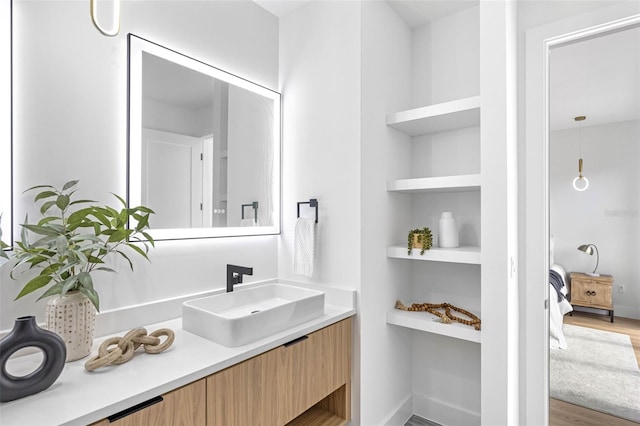 bathroom featuring wood finished floors, built in shelves, connected bathroom, and vanity