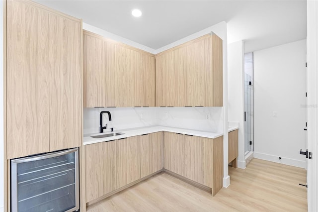 kitchen with wine cooler, a sink, light countertops, light brown cabinetry, and modern cabinets