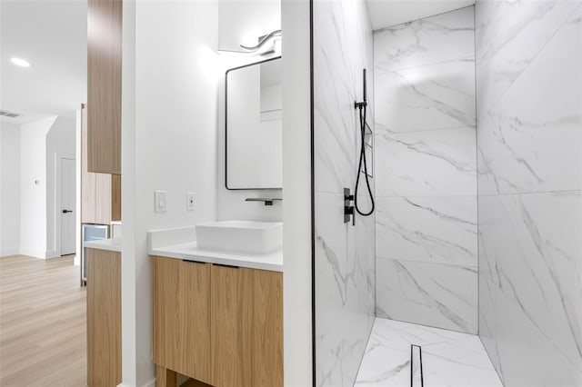 bathroom with a marble finish shower, wood finished floors, and vanity