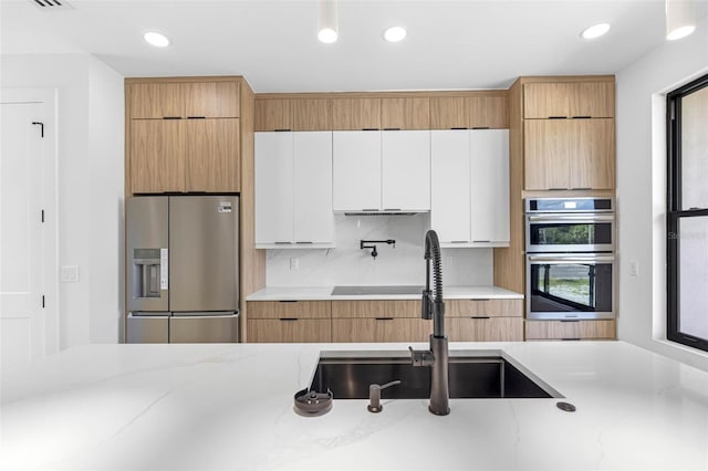 kitchen with light stone counters, appliances with stainless steel finishes, white cabinets, a sink, and modern cabinets