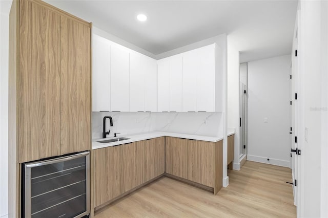 kitchen with wine cooler, light countertops, light wood-style floors, a sink, and modern cabinets