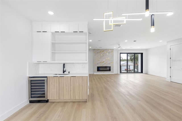 bar featuring light wood-style flooring, beverage cooler, a fireplace, a sink, and decorative light fixtures