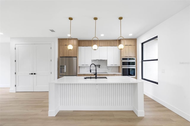 kitchen featuring a center island with sink, appliances with stainless steel finishes, light countertops, white cabinetry, and a sink