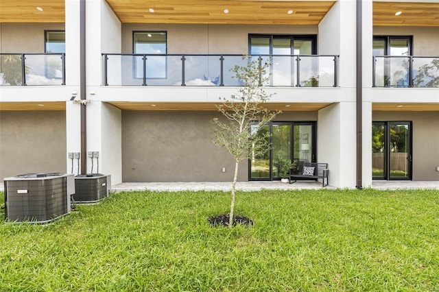 back of property with central AC unit, a lawn, and stucco siding