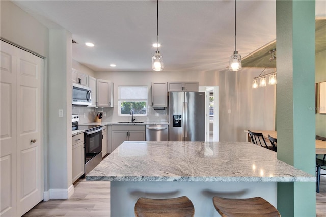 kitchen with stainless steel appliances, a sink, a kitchen breakfast bar, light stone countertops, and decorative light fixtures