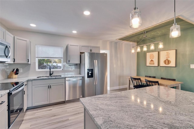 kitchen with light stone counters, stainless steel appliances, a sink, hanging light fixtures, and tasteful backsplash