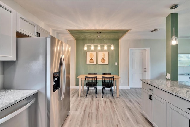 kitchen with stainless steel fridge, white cabinets, light stone counters, decorative light fixtures, and light wood-type flooring