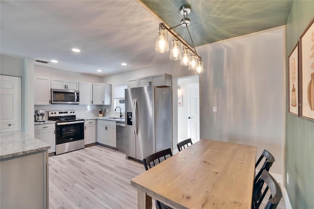 kitchen with light stone counters, pendant lighting, appliances with stainless steel finishes, light wood-style floors, and a sink