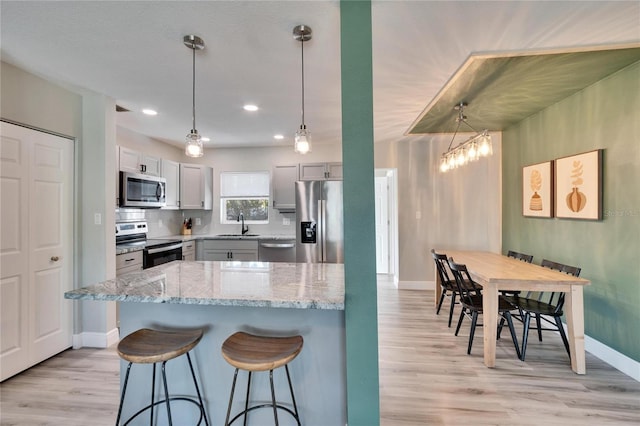 kitchen featuring light wood-style flooring, appliances with stainless steel finishes, hanging light fixtures, light stone countertops, and a sink