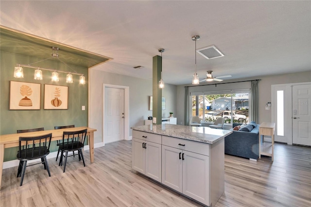 kitchen featuring visible vents, light stone counters, open floor plan, a center island, and white cabinetry