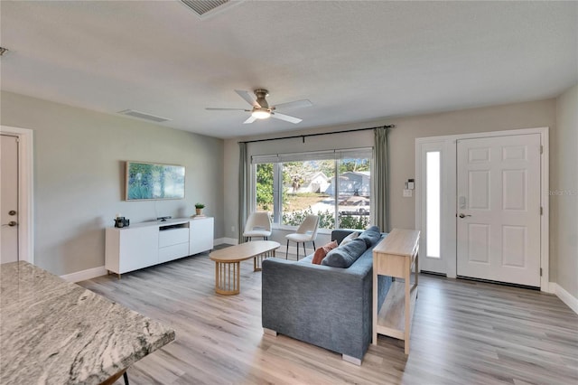 living area with light wood-type flooring, visible vents, ceiling fan, and baseboards