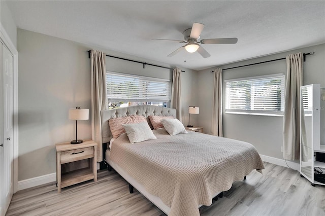 bedroom featuring light wood-type flooring, a textured ceiling, baseboards, and a ceiling fan