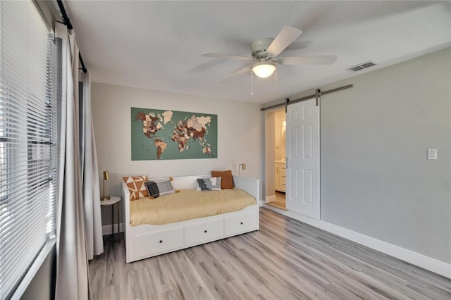 bedroom featuring baseboards, a barn door, visible vents, and light wood-style floors