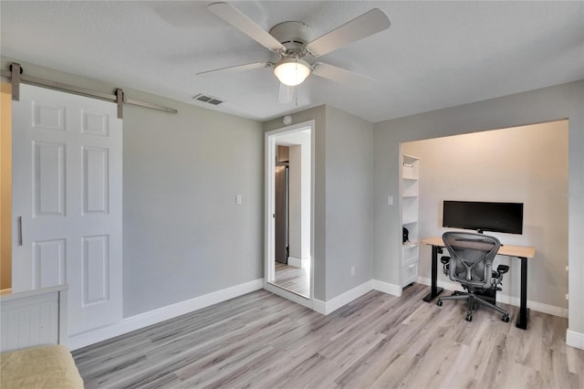 home office featuring light wood finished floors, a barn door, visible vents, and baseboards