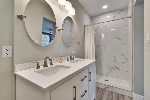 bathroom featuring double vanity, wood finished floors, a stall shower, and a sink