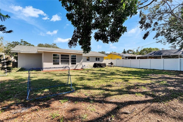 rear view of house featuring fence private yard, a lawn, and stucco siding