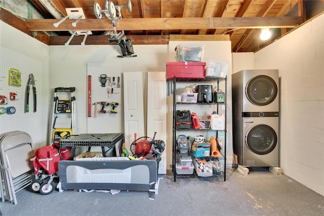 garage featuring concrete block wall, stacked washing maching and dryer, and a workshop area