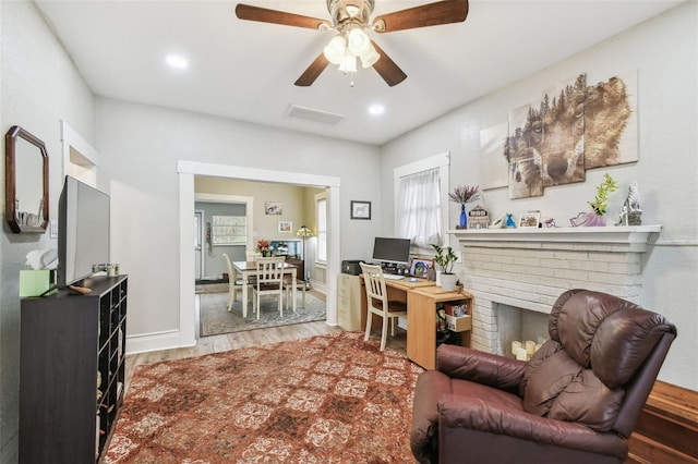 interior space featuring visible vents, a ceiling fan, a brick fireplace, wood finished floors, and baseboards