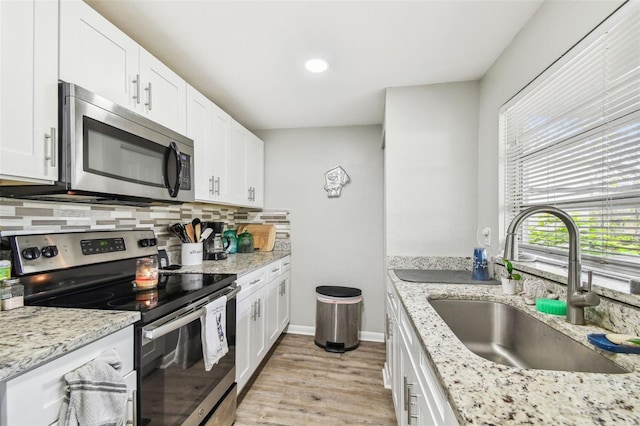 kitchen with light wood finished floors, tasteful backsplash, white cabinets, stainless steel appliances, and a sink