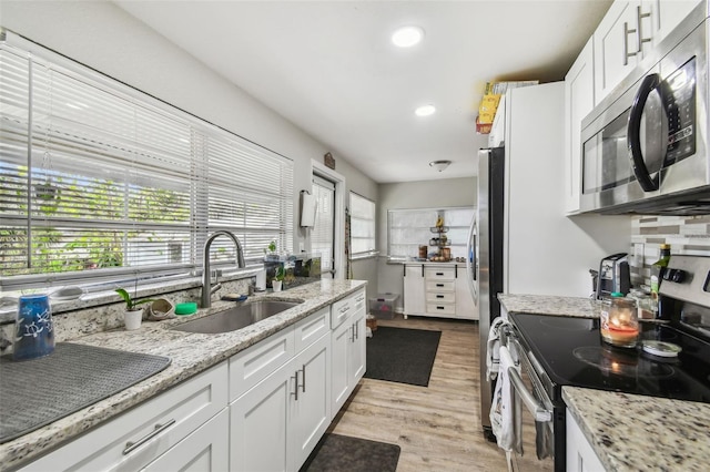 kitchen with appliances with stainless steel finishes, light wood-style floors, white cabinetry, and a sink