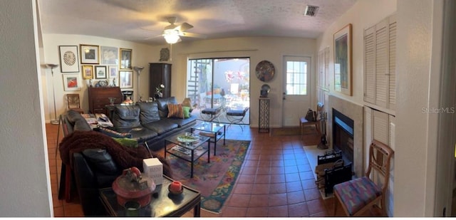 tiled living room with a fireplace with flush hearth, visible vents, a textured ceiling, and a ceiling fan