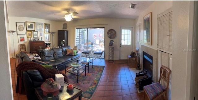 tiled living room featuring a fireplace with flush hearth, visible vents, a textured ceiling, and a ceiling fan