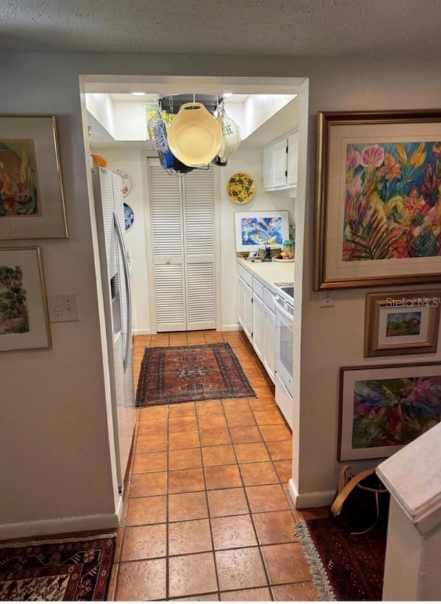 kitchen with white cabinets, white range oven, stainless steel fridge with ice dispenser, and light tile patterned floors