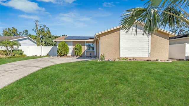 ranch-style home featuring roof mounted solar panels, fence, a front lawn, and stucco siding