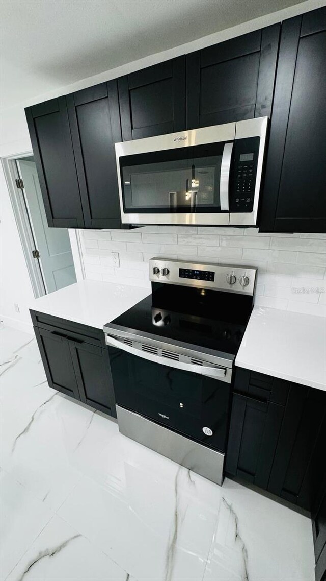 kitchen with marble finish floor, stainless steel appliances, and dark cabinets