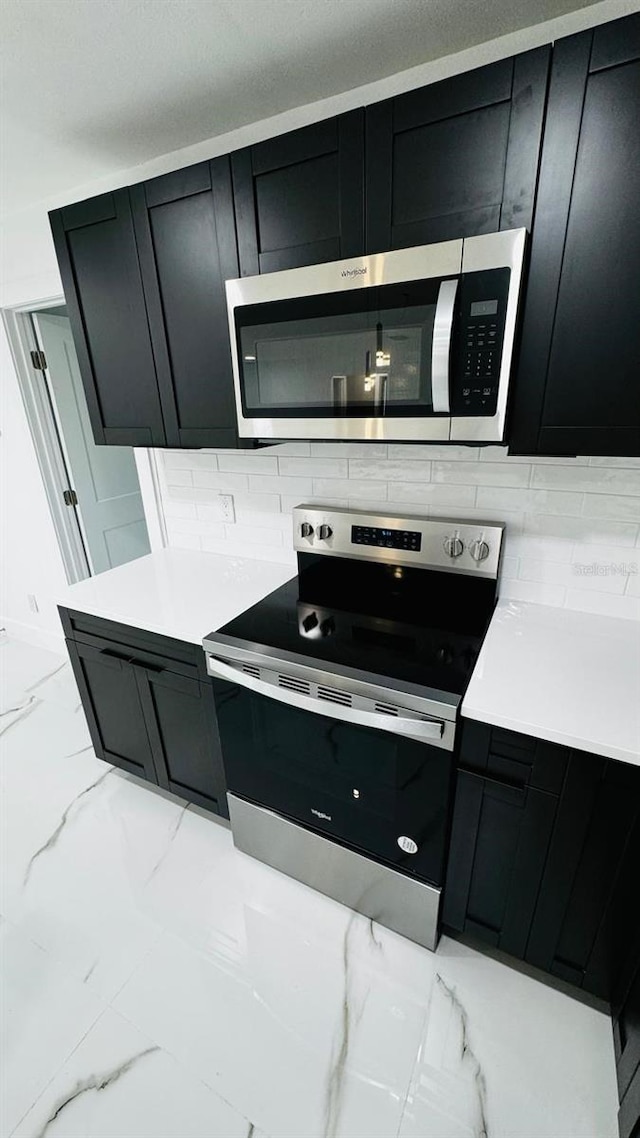 kitchen featuring marble finish floor, light countertops, decorative backsplash, appliances with stainless steel finishes, and dark cabinetry