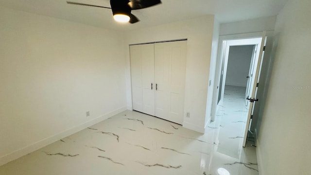 unfurnished bedroom with a closet, marble finish floor, ceiling fan, and baseboards