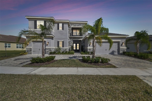 view of front of home featuring a garage, stone siding, decorative driveway, and stucco siding